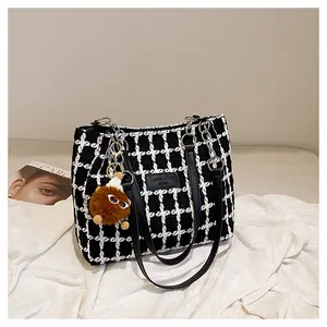 Detail of black and white plaid tweed tote bag with leather straps and plush charm