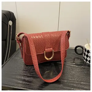 Detail of burgundy woven leather texture with gold horseshoe buckle on crossbody bag