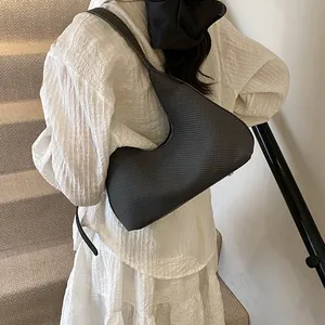 Minimalist dark grey crescent bag with textured grid finish worn as a shoulder bag