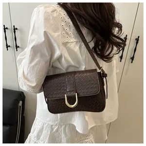 Detail of dark brown embossed shoulder bag with gold horseshoe buckle on white shirt