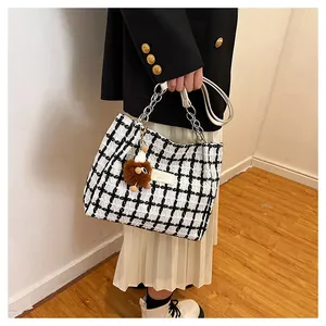 Detail of black and white plaid tweed tote bag with metal chain and plush ball charm