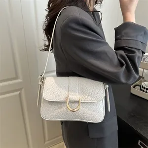 Chic white woven shoulder bag with gold D-ring buckle, worn with a charcoal blazer