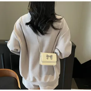 Gros plan du mini sac crème avec nœud argenté et bandoulière en chaîne métallique