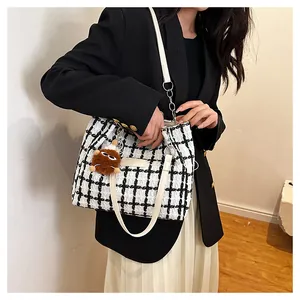 Close-up of black and white plaid tweed tote bag with plush charm and white straps