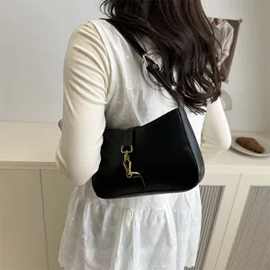Retro black leather underarm bag with gold metal buckle shown on a model in a minimal setting