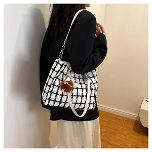 Detail of checkered tweed tote bag with white leather strap and plush charm on model