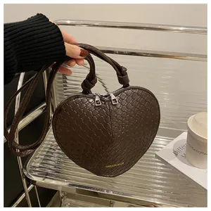 Detail of dark brown woven leather heart-shaped bag with knot handles and gold lettering