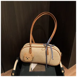 Détail d'un sac à bandoulière en paille avec ours en peluche et ruban à carreaux