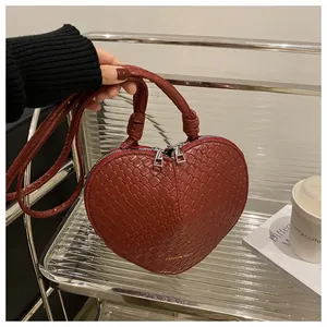 Detail of red heart-shaped handbag featuring woven texture and silver double zippers