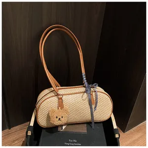 Détail du sac cylindrique tissé avec anses brunes, ruban bleu et breloque en forme d'ours