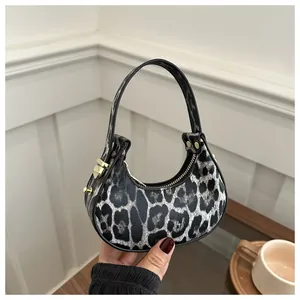 Détail du sac croissant à motif léopard avec poignée noire et finitions métalliques dorées