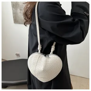 White heart-shaped crossbody bag with crocodile pattern and knotted strap on model
