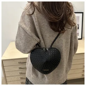 Detailed back view of a black woven heart-shaped crossbody bag worn by a model