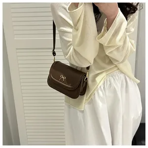 Detail of dark brown leather crossbody bag with a golden bow buckle on a side view model