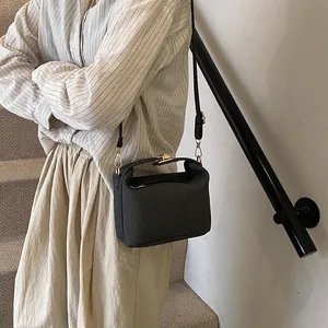 Elegant black woven Lindy shoulder bag with gold hardware worn by a model on stairs