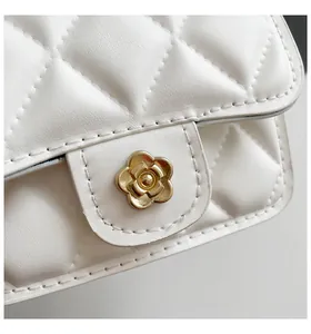 Detailed view of the gold flower-shaped metal clasp on a white quilted shoulder bag