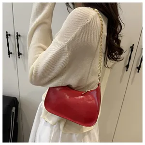 Detail view of the red glossy crescent bag with gold chain strap on a female model