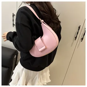 Side view of a pink crescent hobo bag with wide strap worn on a woman's shoulder