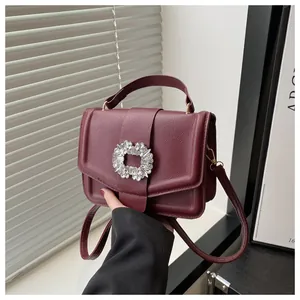 Detailed view of wine red lychee leather handbag with a large sparkling rhinestone buckle