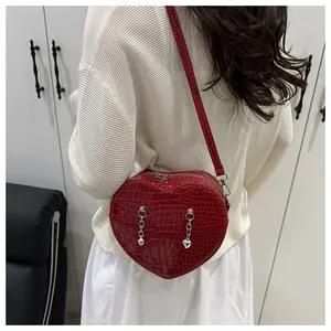 Detail of red heart-shaped crossbody bag with crocodile pattern and silver chain pendants