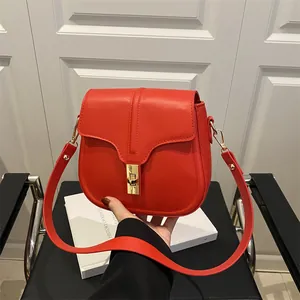 Stylish red saddle shoulder bag with golden buckle held by a model in modern setting