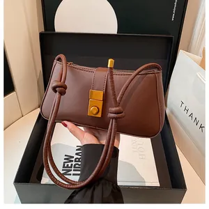 Close-up of a brown leather shoulder bag with a gold buckle and twisted strap in a gift box