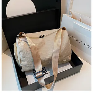 Gros plan d'un sac messager en nylon beige avec broderie FY dans une boîte cadeau
