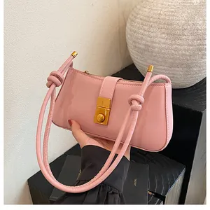 Detailed close-up of pink glossy shoulder bag featuring a gold clasp and knot strap