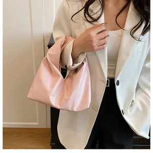 Rosafarbene Falten-Eimertasche mit Knotendesign, getragen von einem Modell im weißen Anzug