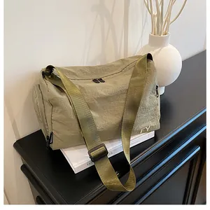 Sac bandoulière en nylon olive avec logo FY posé sur un livre, décor intérieur