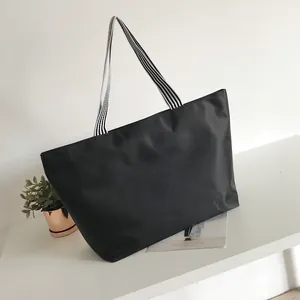 Detail of waterproof black tote bag with striped fabric handles on white surface