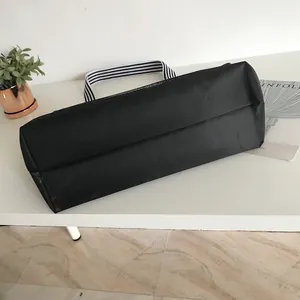 Flat lay of black tote bag showing wide base and black-white striped strap on desk
