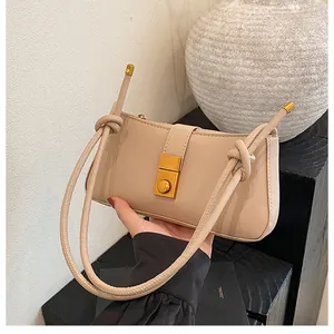 Detail of minimalist beige underarm bag showing golden twist lock and knotted strap