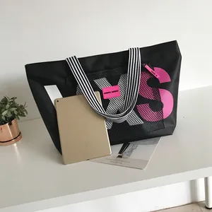 Close-up of black nylon tote bag with mesh pockets, pink rubber logo and striped handles