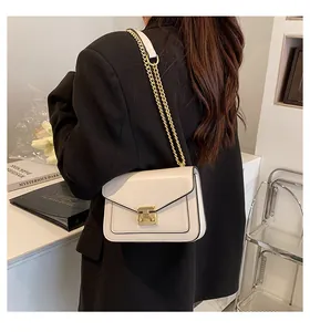 Detail of cream crossbody bag with gold rectangular clasp and chain strap over black blazer