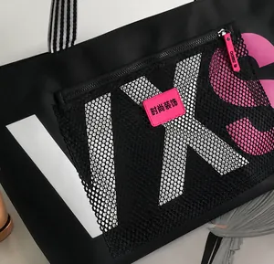 Detail of black tote bag featuring mesh pocket with pink logo and white letter printing