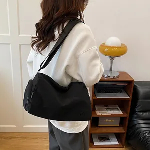 Grand sac messager en nylon noir avec large bandoulière porté par un mannequin