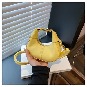 Détail d'un sac demi-lune jaune avec bandoulière et ferrures dorées tenu à la main