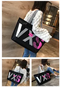 Close-up of black tote bag featuring VXS letter print and pink decorative labels