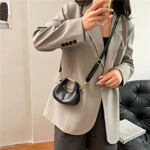Mini sac demi-lune noir chic avec détails dorés et bandoulière réglable porté par un mannequin