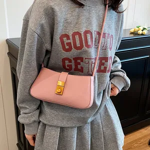 Pink rectangular leather underarm bag with gold metal clasp on a grey sweatshirt backdrop