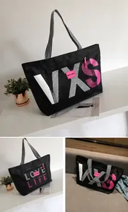 Detail of black nylon travel tote with mesh pocket and pink logo on a white display stand