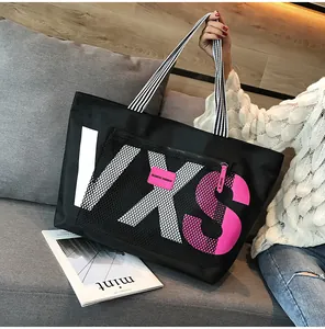 Detail of black tote bag with mesh pocket and colorful VXS lettering on a sofa