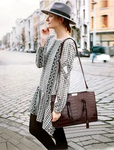 Close-up of a large dark brown crocodile pattern tote bag with gold logo in street setting