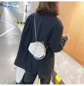 Λεπτομέρεια λευκού clutch με πέρλες, χρυσό πλαίσιο και κομψή αλυσίδα ώμου