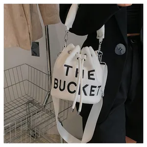 Chic white plush bucket bag with bold THE BUCKET lettering and wide shoulder strap