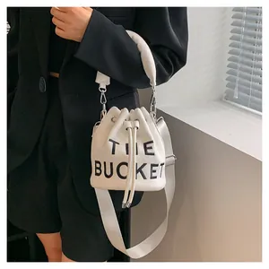 Detailed shot of white plush bucket bag featuring black The Bucket text and strap