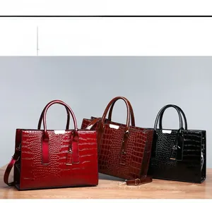 Detailed view of crocodile pattern tote bags in red, brown, and black with leather straps