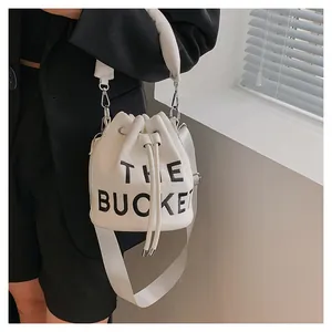 Detail view of the white plush bucket bag showing the large printed black THE BUCKET text