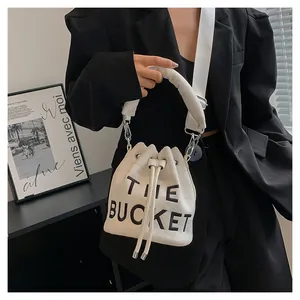 Detailed view of white bucket bag with THE BUCKET text and black blazer background